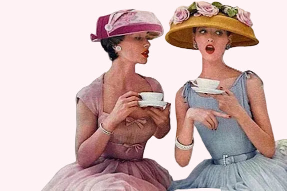 Two women in vintage dresses and hats holding tea cups against a plain background