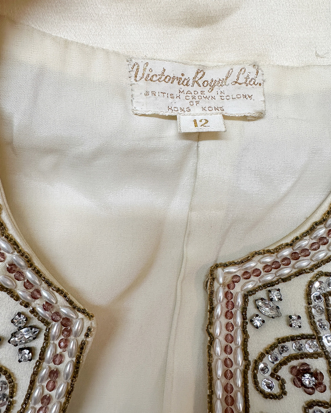 Close-up of a garment with 'Victoria Royal Ltd.' label and size tag, featuring intricate beadwork.