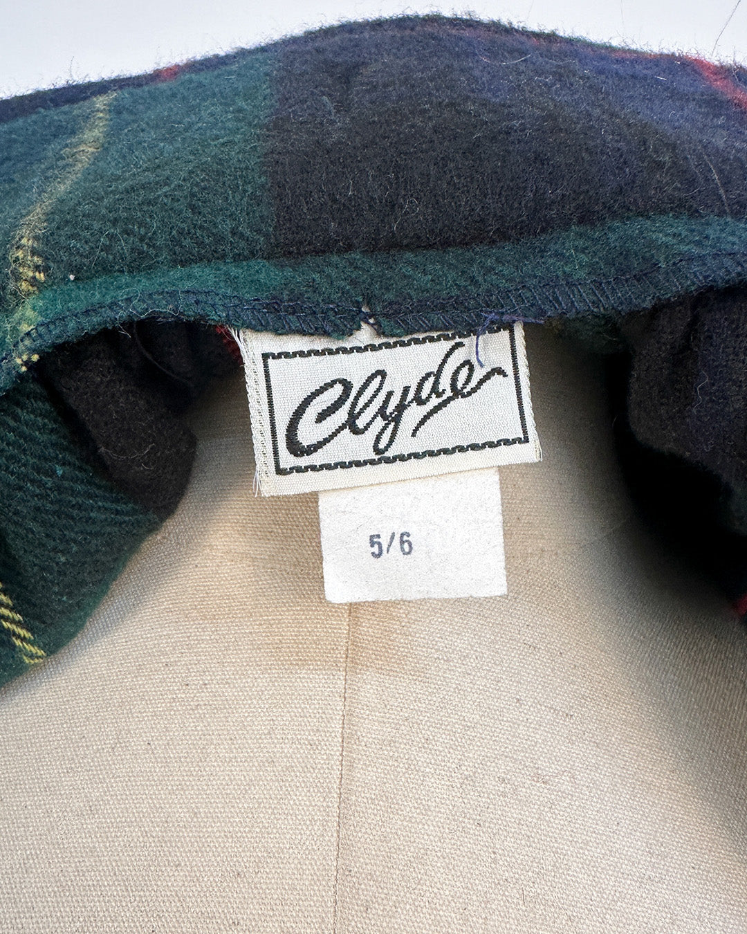 Close-up of a plaid fabric with a 'Clyde' label and size tag on a neutral background