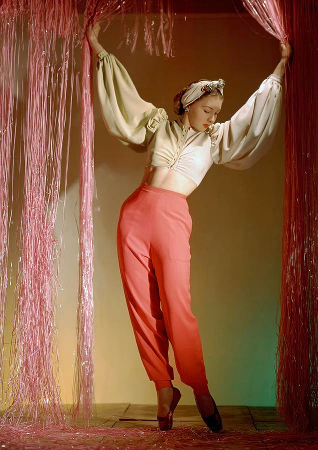 Person in a white blouse and red pants standing between two red curtains.
